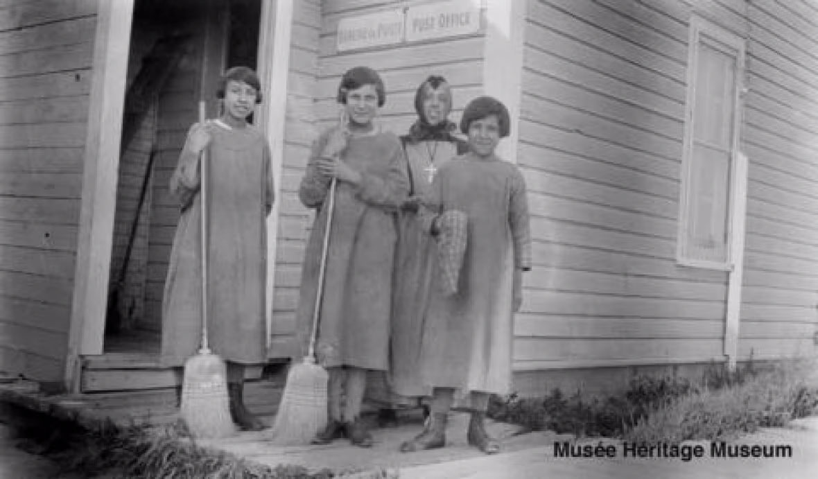 Three girls and Sister Aldea Gagnon in front of the Saddle Lake Post Office.