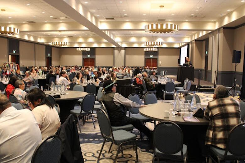 A large conference room full of people sitting around circular tables.
